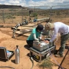 two women working at a machine in the desert